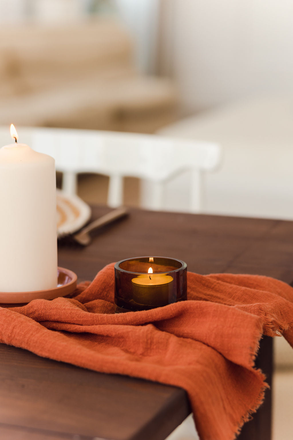 close up of maison table runner in terracotta colour with a amber votive candle on a dark wood table