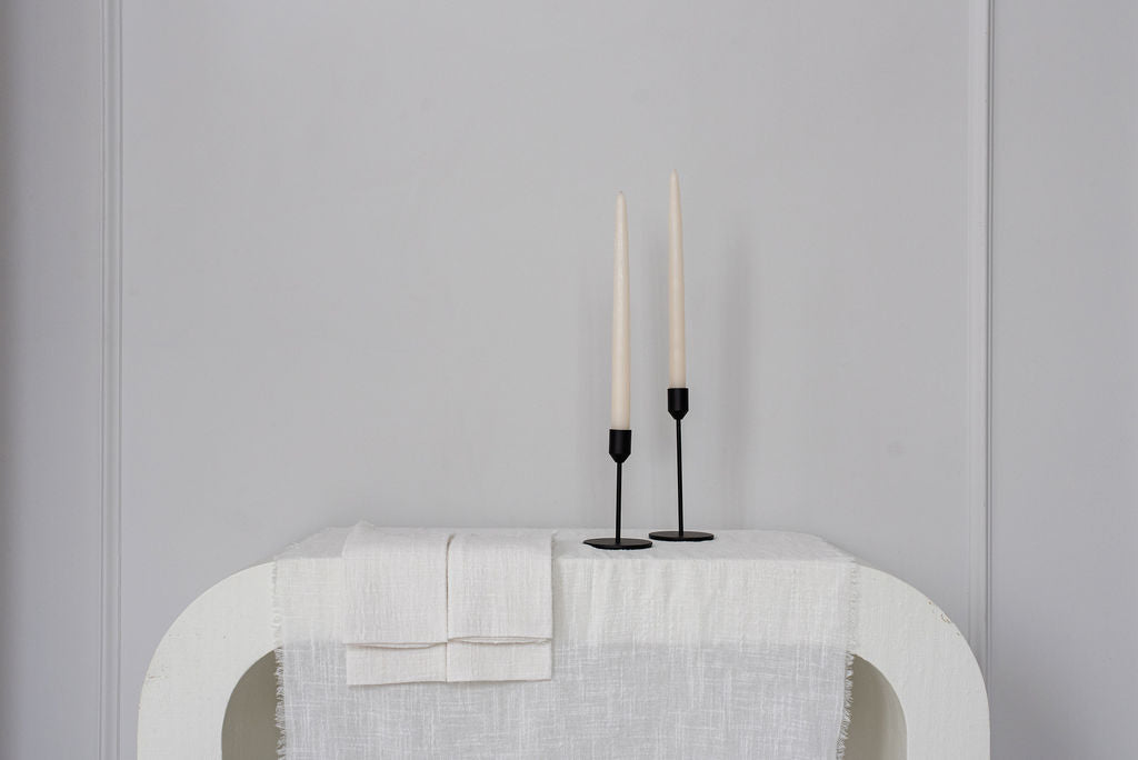 black candle holders standing on white side table with white linens drapped over table
