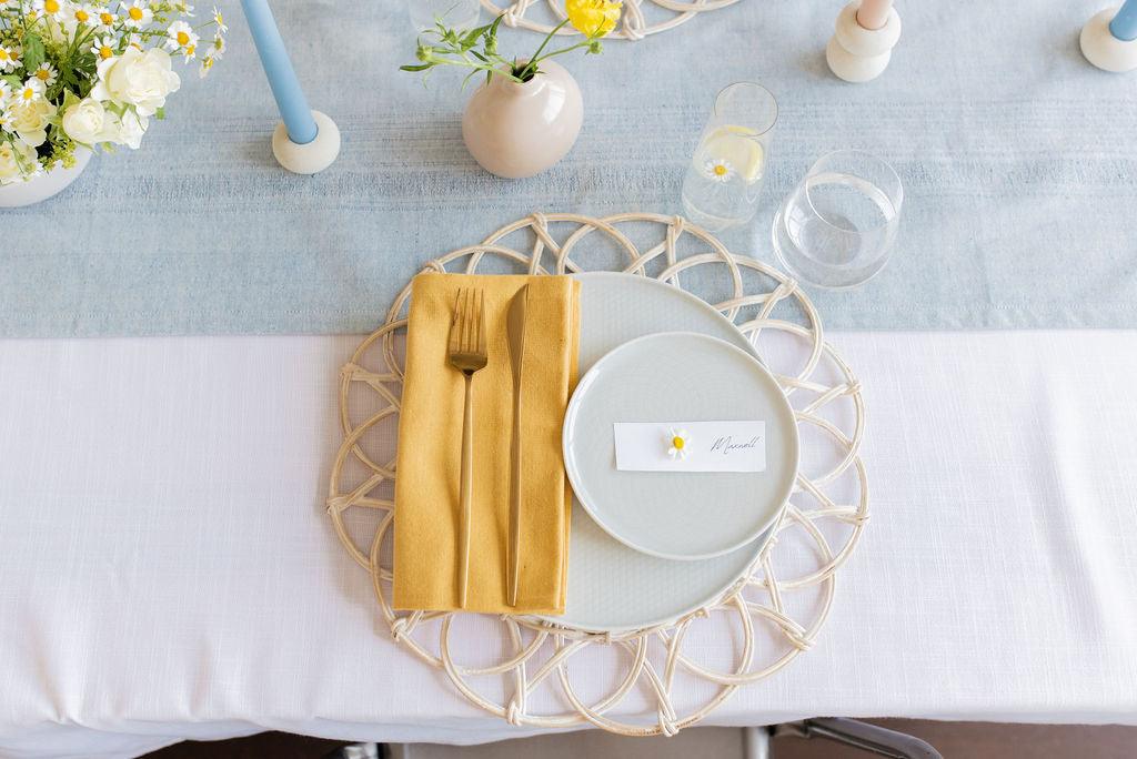 solid yellow cotton napkin folded to the left ontop of light coloured table setting