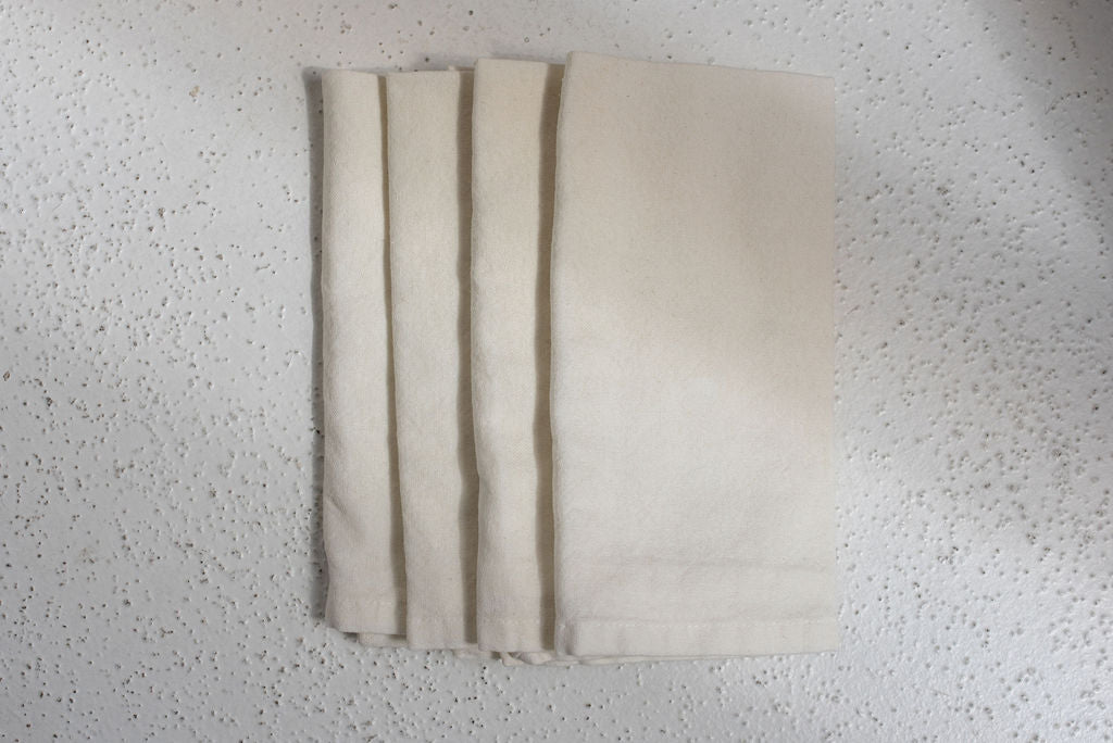 close up of four folded ivory cotton dinner napkins centered in photo on white textured surface