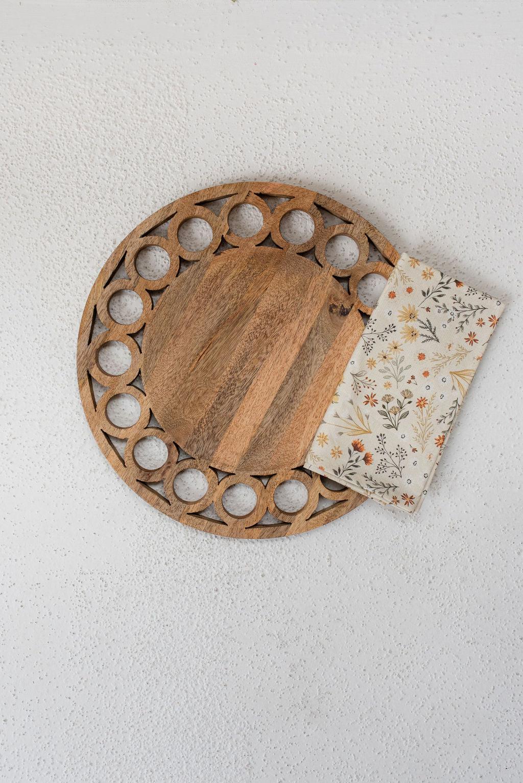wooden circle charger centered on white texured surface with fall meadow napkin folded overlapping charger