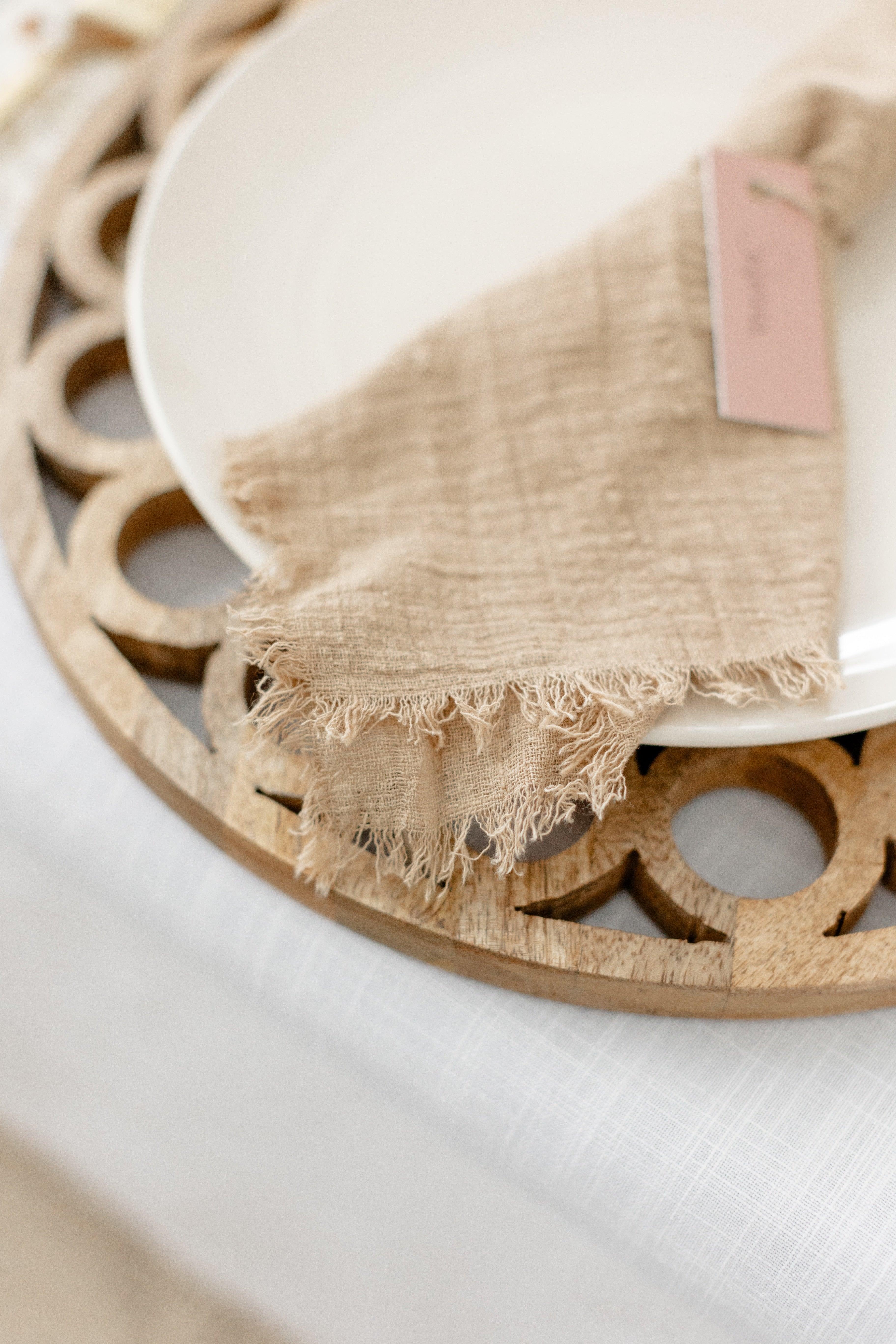 close up of wooden circle charger with white plate and natural linen napkin ontop