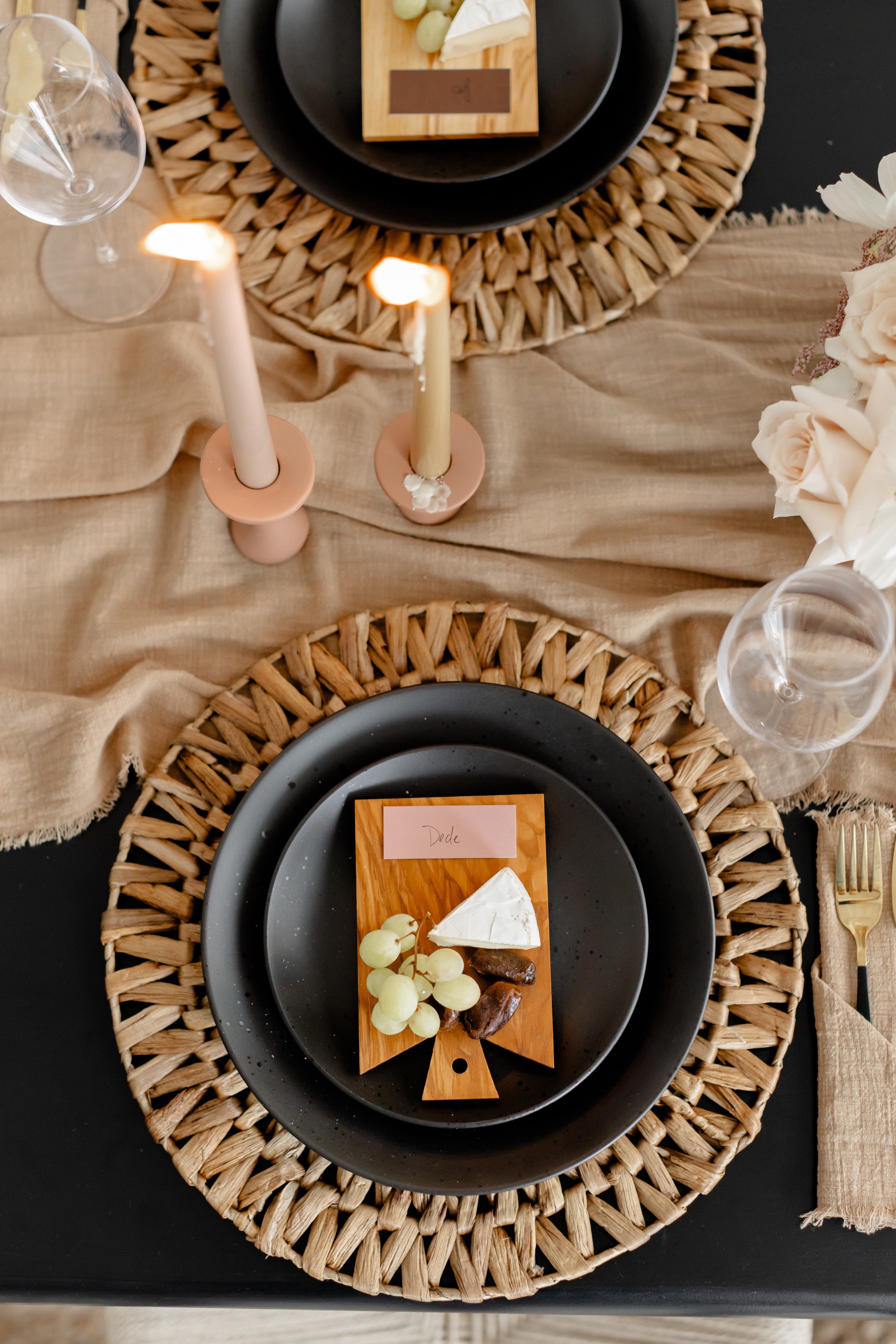 black table with neutral textured linens lit candles and havest printable place card on black plate with cheese and grapes