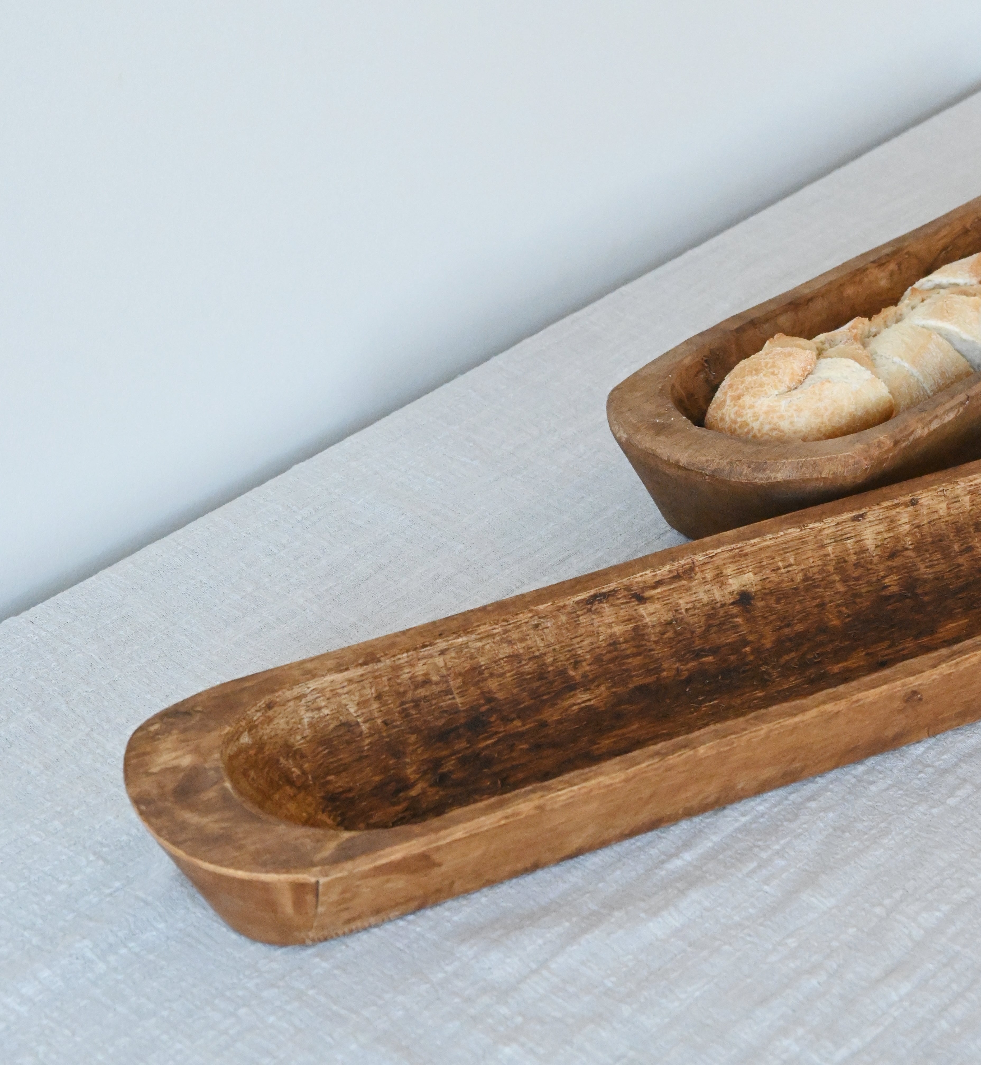 close up of two  mango wood baguette holders sitting on an oatmeal gauze table runner