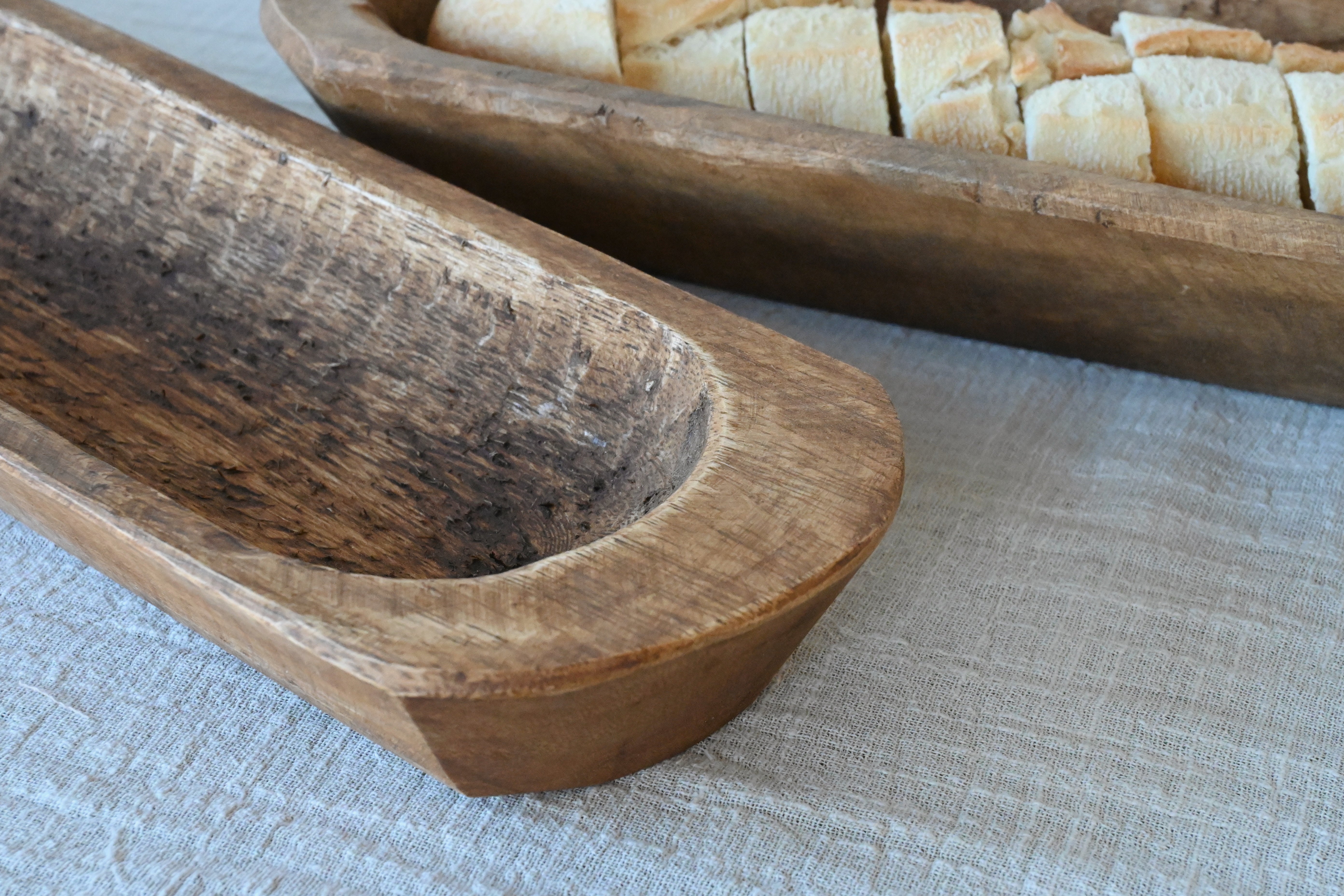 detail shot of two  mango wood baguette holders sitting on an oatmeal gauze table runner