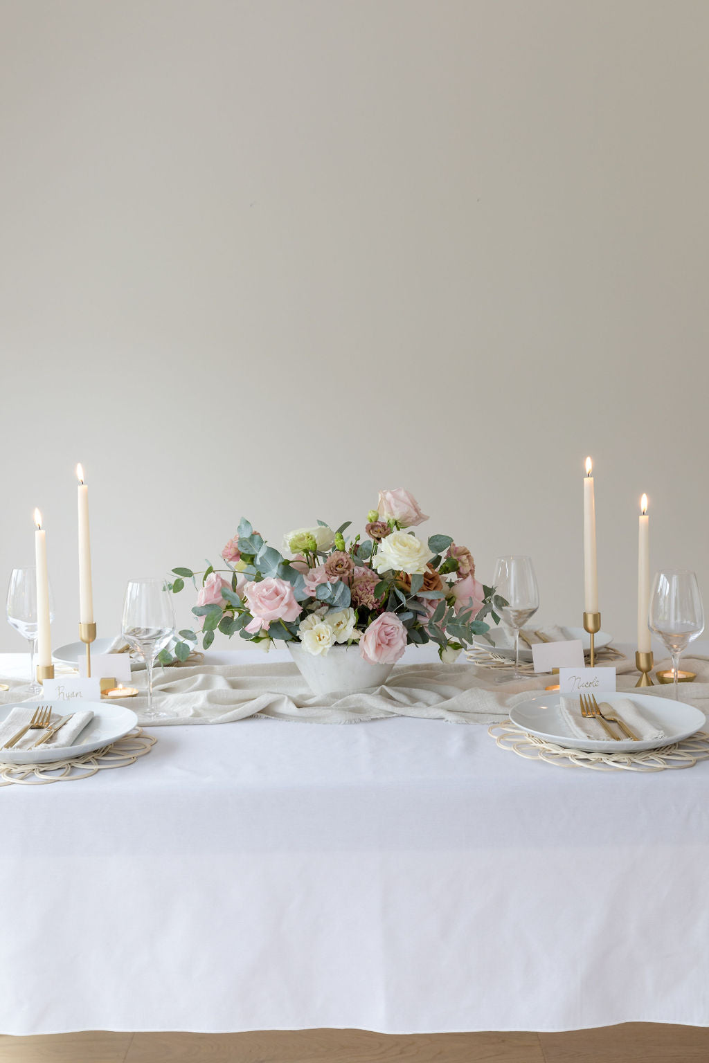 white table cloth, pink and white floral arrangement at the centre of the table and four golden light taper candle holders