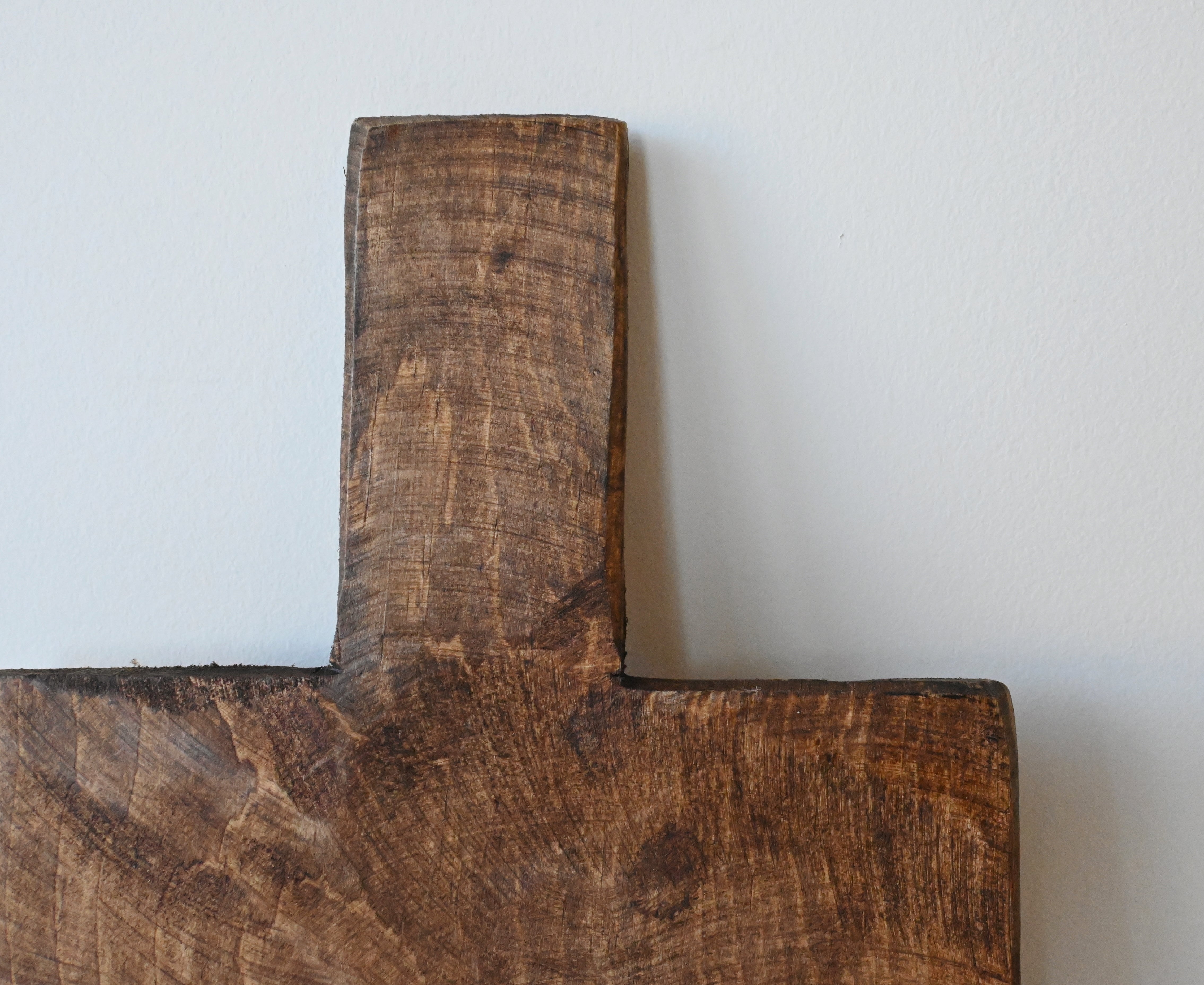 close up of  dark square mango wood cutting or charcuterie board  handle. The board is leaning against a white wall