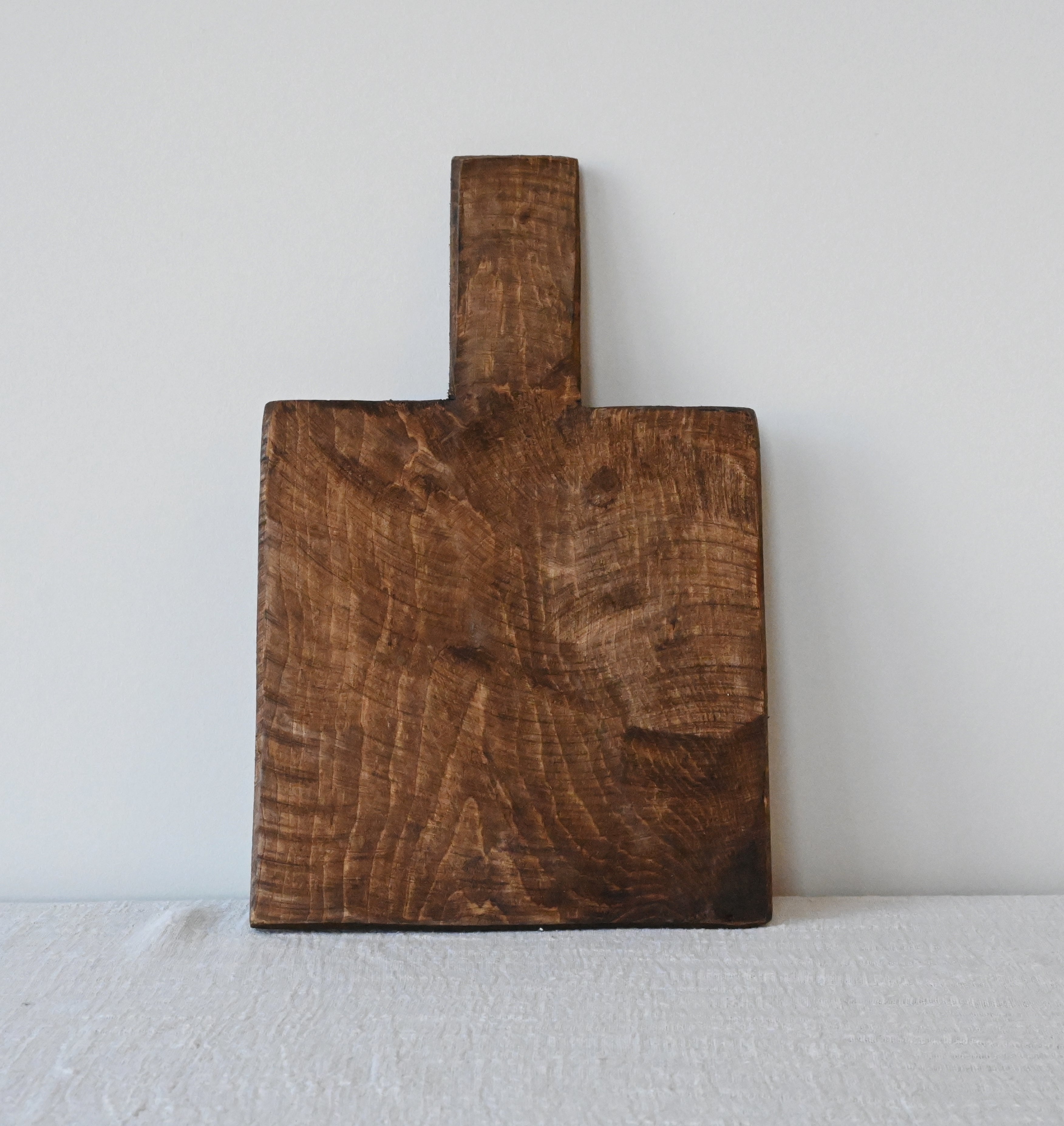 one dark square mango wood cutting or charcuterie board leaning against a white wall