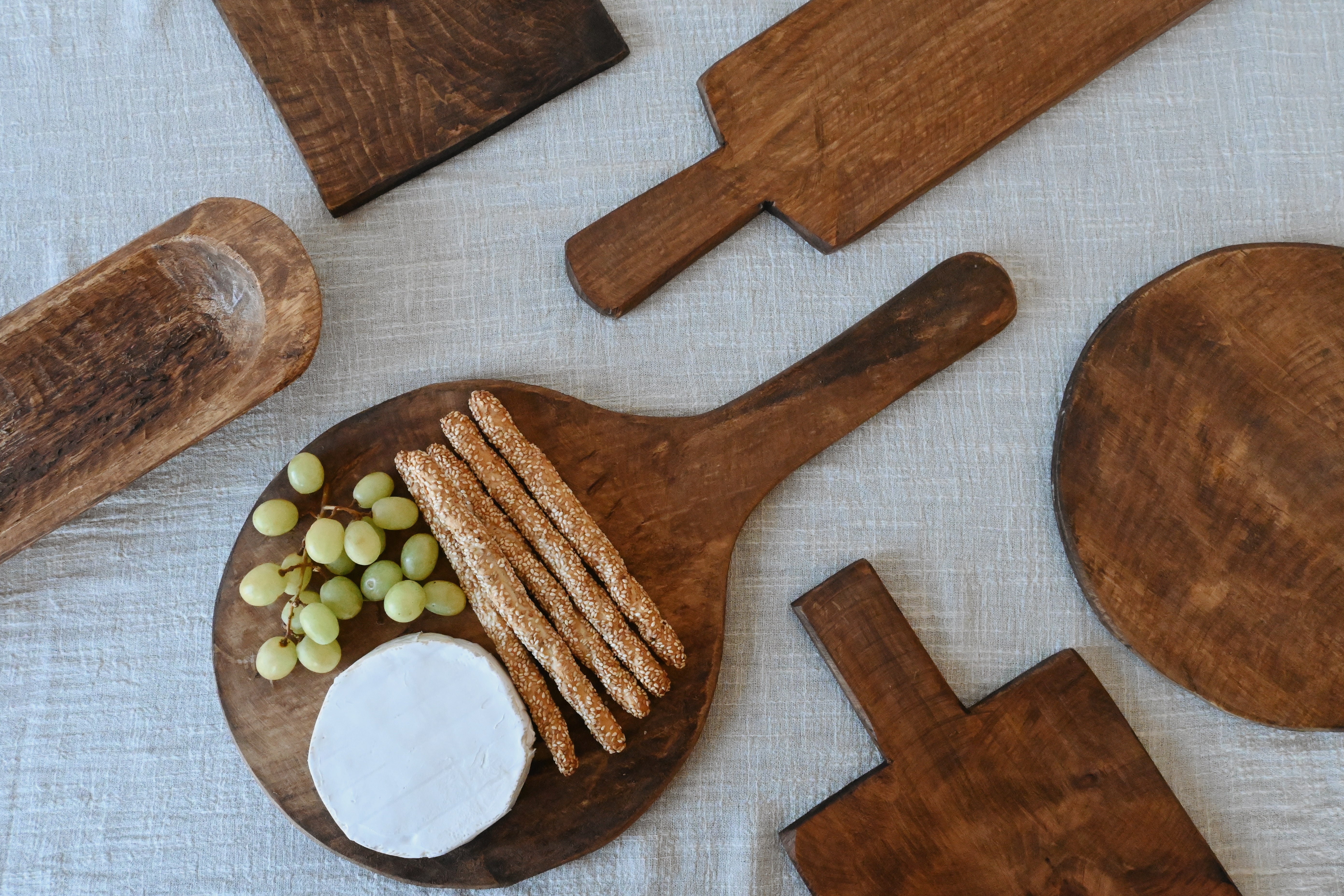 an flatlay of mango wood handcrafted  charcuterie boards. A mix of long, round and sqaure boards as well as a wooden baguette holder.