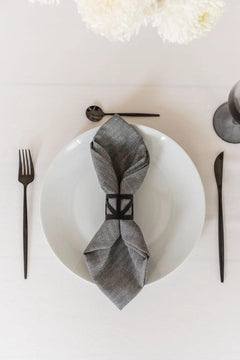 Black metal napkin ring holding a grey napkin sitting on a white plate with black cutlery