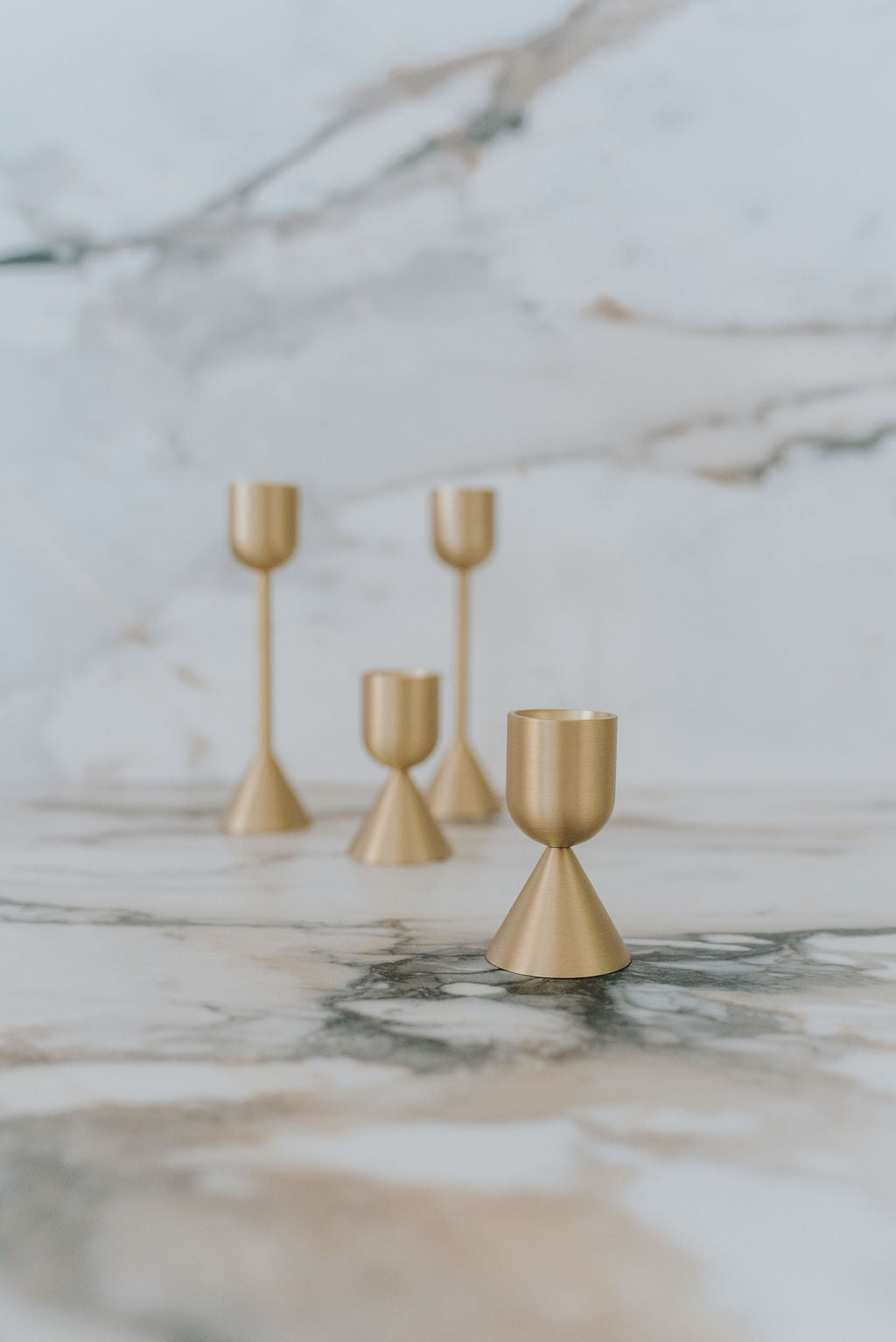 golden metal candle stick holders in 2 different heights on a marble countertop