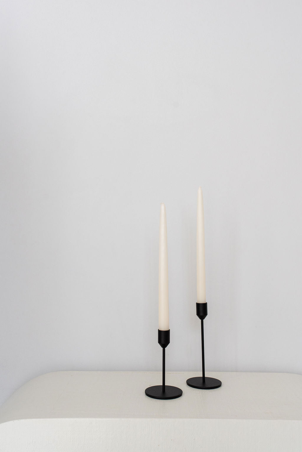 black candle holders different heights on white table with white background