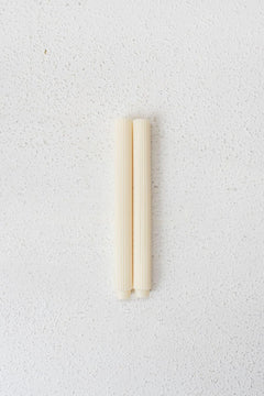 pair of cream coloured roma candles centered on textured white surface