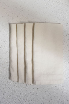four folded ivory cotton dinner napkins centered in photo on white textured surface