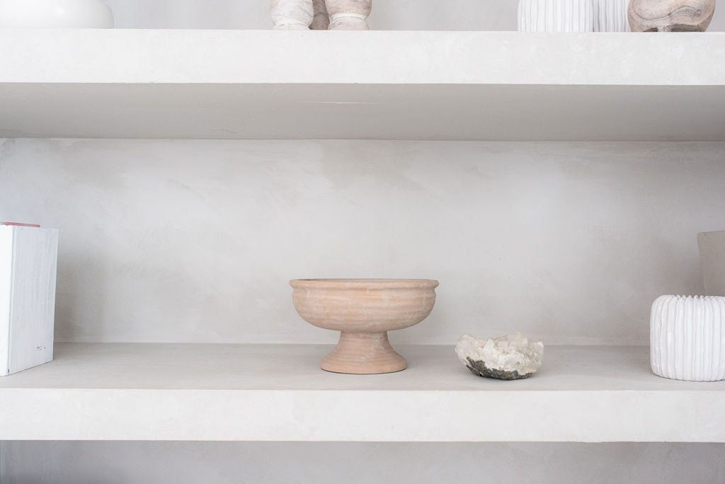 single rustic pedestal vase on natural textured shelf with white knick knacks on surrounding shelves