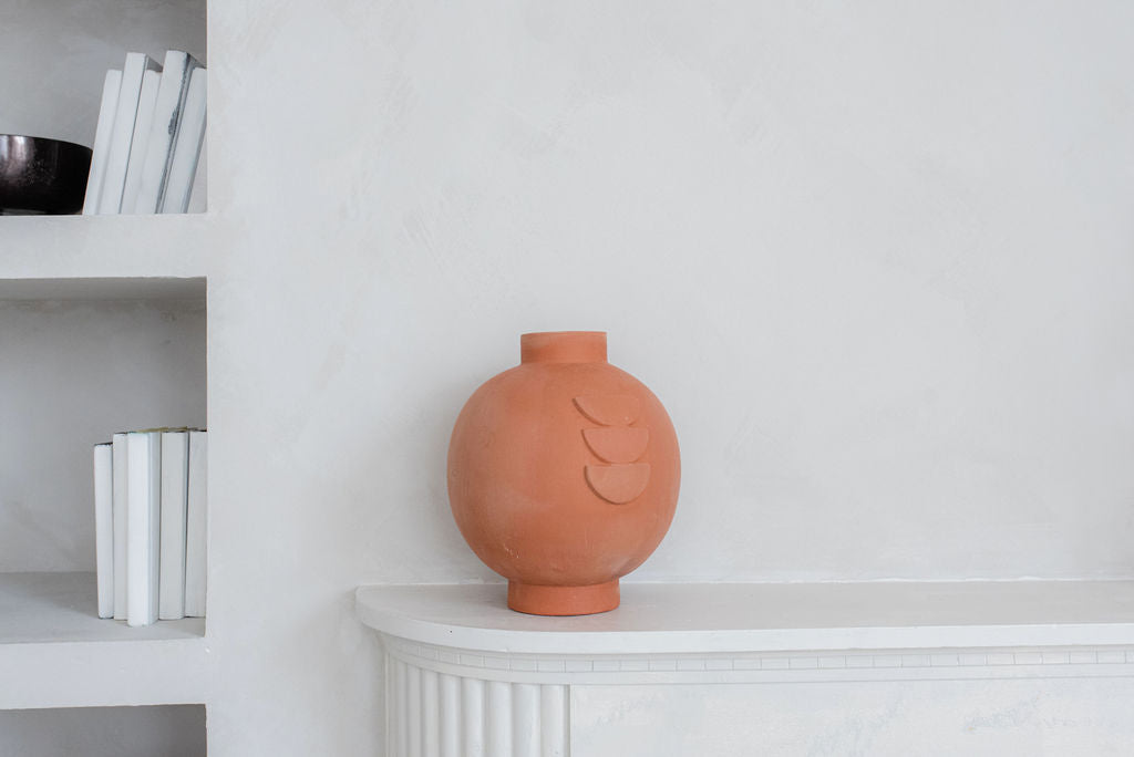 single terracotta vase on white side table bookshelf to the left of the side table