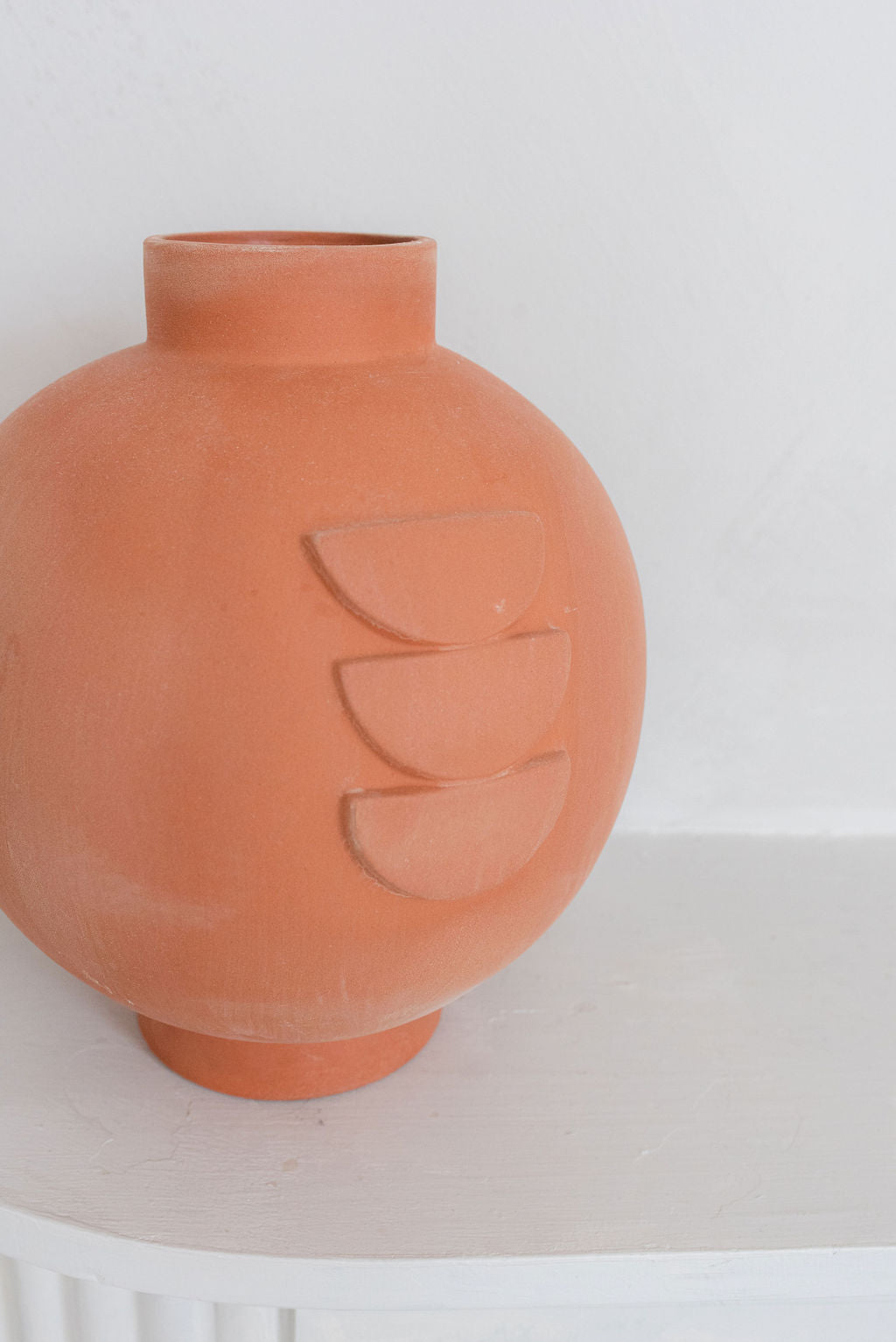 close up of single terracotta vase left side of photo on white table with white background