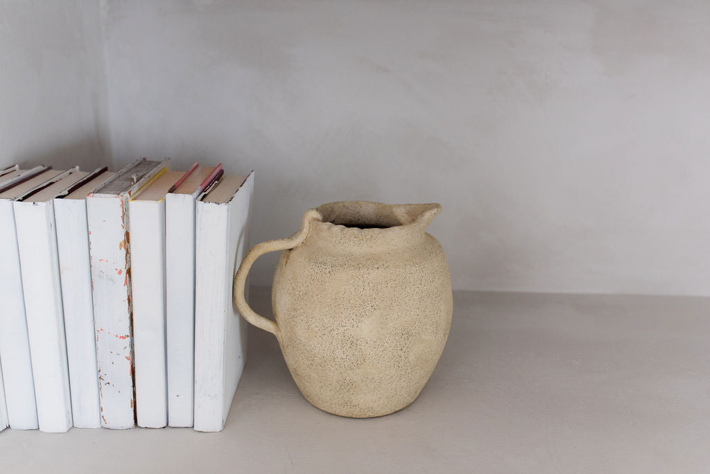 close up of single vintage jug vase holding up seven white books on the left side of shelf