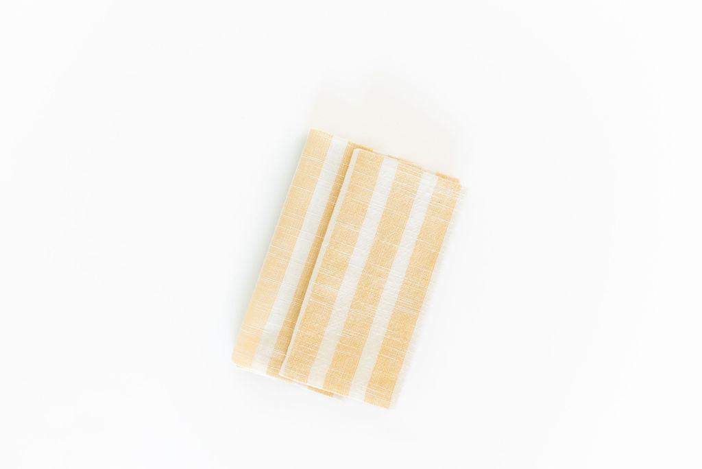 two folded yellow striped cotton napkins on an angle white background