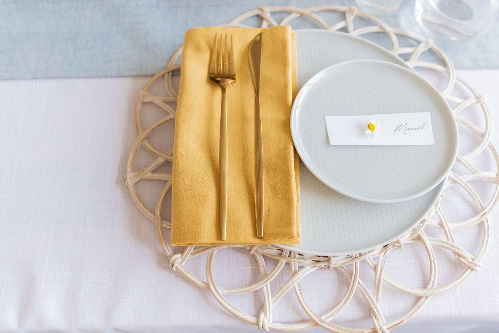 close up of solid yellow cotton napkin folded to the left ontop of light coloured table setting