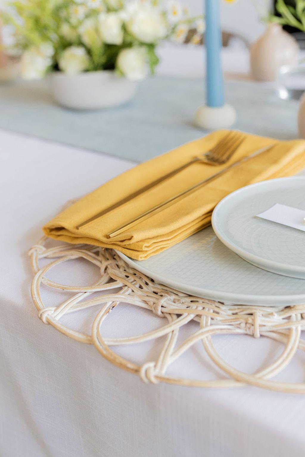 angled close up of solid yellow napkin on light coloured table setting