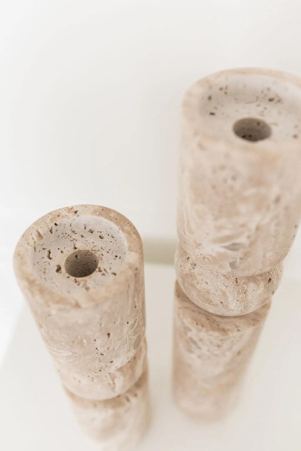 two travertine candle holders sitting on a white stand showing candle opening
