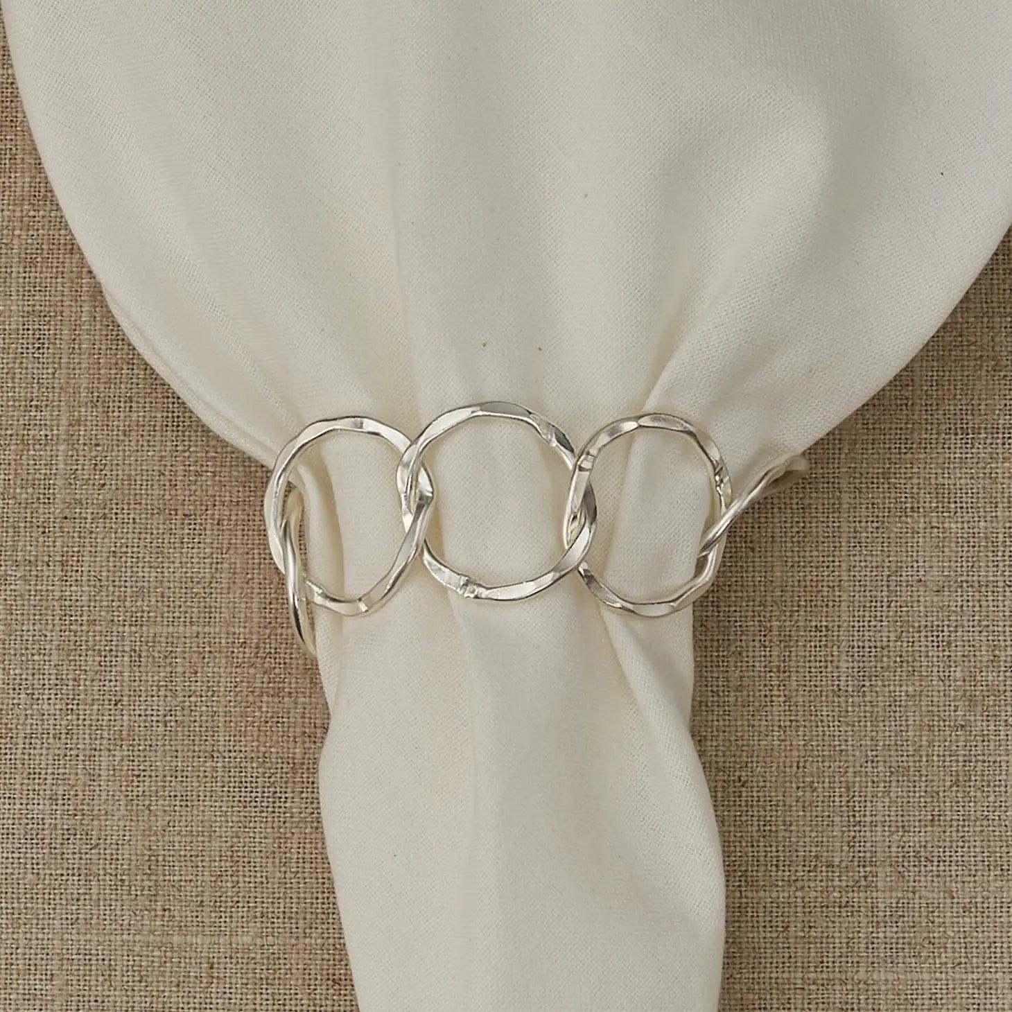 silver chainlink metal napkin ring white napkin with beige textured fabric background