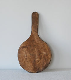 round charcuterie or cutting board with a handle standing up against a white wall